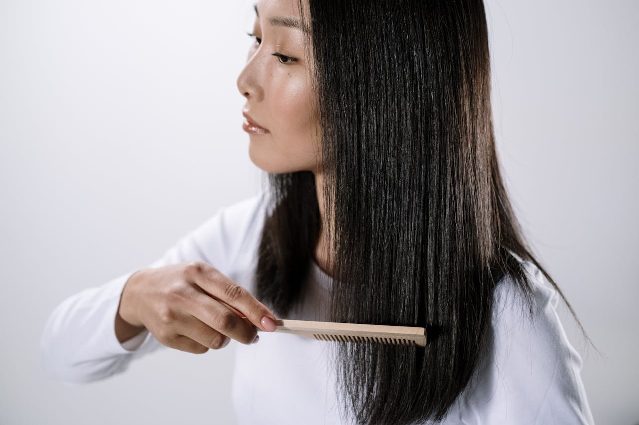 hero-img-02 Studio portrait of an Asian woman combing her straight black hair indoors with a white background.