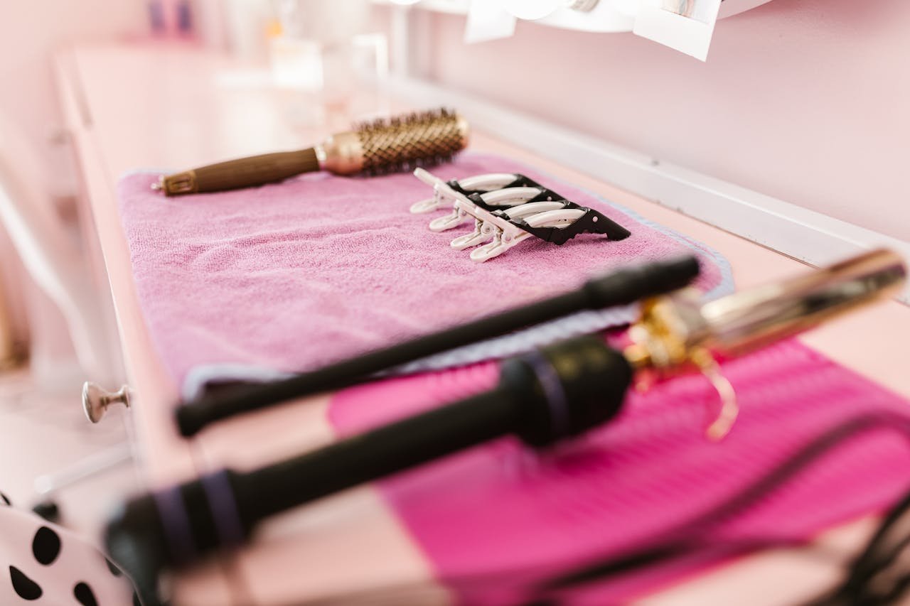 gallery-1 A selection of hair styling tools arranged on a pink towel in a salon setting, ready for use.